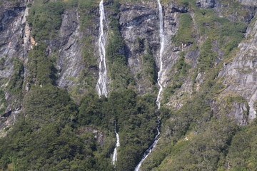 wąskie i wysokie wodospady los amigos w Ushuaia spływające po wysokich stromych ścianach skalnych pokrytych fragmentarycznie roślinnością  - obrazy, fototapety, plakaty