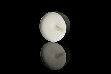 One whole waxy white tea candle isolated on black glass