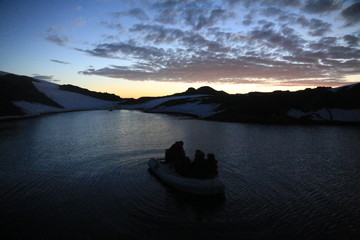 ludzie na łodzi motorowej wpływający wieczorem do zatoki u wybrzeży antarktydy - obrazy, fototapety, plakaty