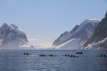 ludzie na łodzi motorowej pomiędzy krami i górami lodowymi wpływający do zatoki u wybrzeży antarktydy - obrazy, fototapety, plakaty