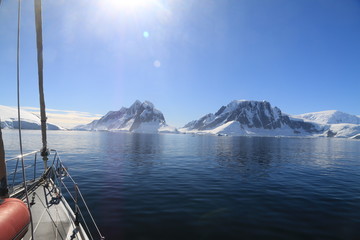 widok z jachtu na spokojne zimne wody oraz górzyste i ośnieżone wybżeże antarktydy - obrazy, fototapety, plakaty