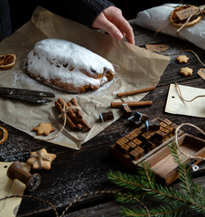 tasty homemade traditional christmas dessert stollen with dried berries and nuts on parchment in woman hand on wooden rustic table with spices, orange slices, Christmas tree branches, selective focus