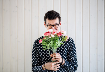 Young man with flowers standing against white wooden background wall.