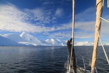 samotny człowiek stojący przy maszcie na łodzi, płynący po zimnych wodach okołobiegunowych z lodowcem w tle - obrazy, fototapety, plakaty