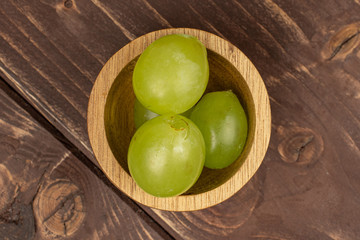 Group of three whole fresh green grape with wooden bowl flatlay on brown wood