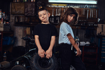 Dream team in action - two kids are having fun while posing for photographer at auto workshop.