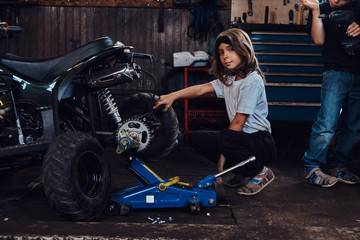 Fototapeta na wymiar Serious beautiful girl want to be an auto technician when she grows up, she is trying to fix broken ATV.
