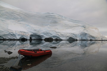 czerwony ponton przycumowany do brzegu na spokojnej wodzie i ośnieżona góra w tle
