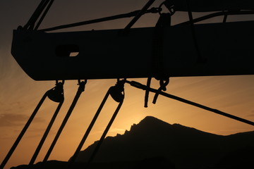 kontury lądu i zachód słońca widziane zza elementów wyposażenia płynącego jachtu