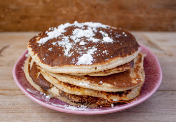 Stack of homemade clean eating oat pancakes with powered sugar on pink plate on rustic country table. Selective soft focus. Shrovetide, pancake carnival maslenitsa concept