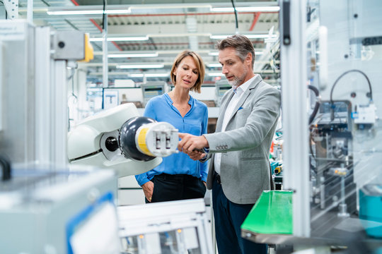 Businessman with tablet and woman talking at assembly robot in a factory