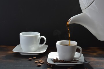 Coffee being poured into small white coffee cups in front of a black background