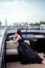 Young beautiful woman in a long silk black dress posing on a yacht. Luxurious life style, summer time