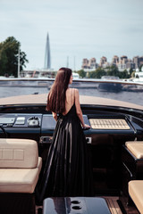 Young beautiful woman in a long silk black dress posing on a yacht. Luxurious life style, summer time