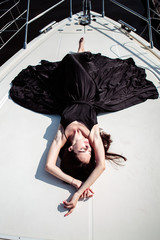 Young beautiful woman in a long silk black dress posing on a yacht. Luxurious life style, summer time