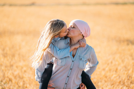 A woman with cancer carrying her daughter on her back, kissing