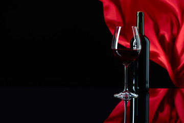 Wineglass and bottle of red wine on a black reflective background.
