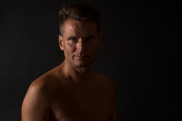Fototapeta na wymiar Portrait of mature man with naked torso in split light