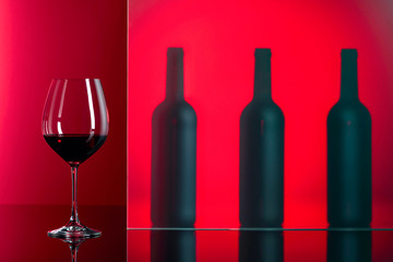 Bottles and glass of red wine on a red background.