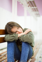 Unhappy depressed teenager with face in hands sitting on the bench