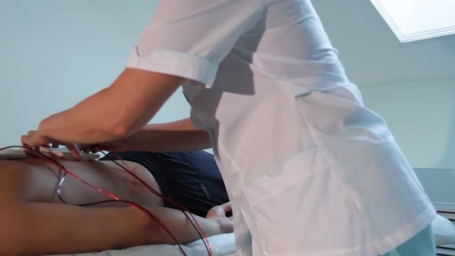 A reflexologist fixes electrodes on the patient's back for electrostimulation
