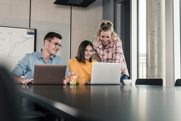 Happy colleagues with laptops meeting in conference room