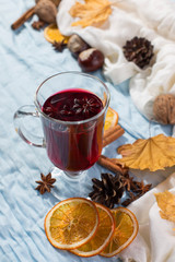 A cup of mulled wine with spices, dry leaves and oranges on the table. Autumn mood, a method to keep warm in the cold, copy space, morning light.