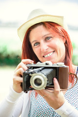 Portrait of a pretty smiling red-haired woman taking pictures with an old camera.