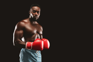 Athletic fighter with red gloves on posing over black background