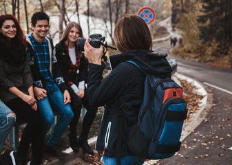 Young woman is taking a photo of her friends on digital camera at autumn forest.