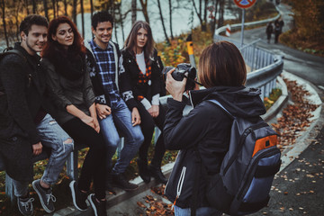 Young woman is taking a photo of her friends on digital camera at autumn forest.