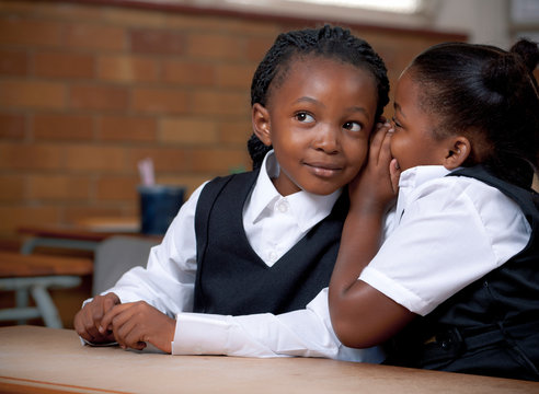 Young African schoolgirl whispering into her friends ear