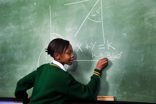 A young girl solving a math sum on a blackboard