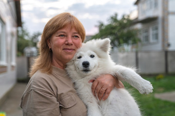 Close up portrait of happy smiling blonde woman that holds white samoyed puppy on her hands