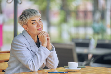 short-haired business woman in a white coat in a street cafe