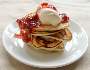 Fresh hot pancakes stack with strawberry jam and sour cream on white plate on natural light linen tablecloth background. Soft focus. Copy space. Pancake carnival maslenitsa breakfast concept