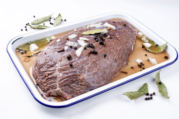 Marinated traditional German Sauerbraten from beef with onion and spice as closeup in a white skillet - isolated