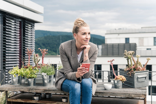 Businesswoman with cell phone sitting on roof terrace having a break