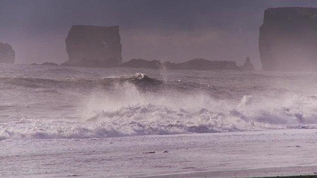 Wide, waves crash past rock formations in Iceland