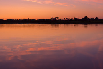 Sunrise at the border of the Netherlands and Belgium. Two countries split by the river Meuse. Picture taken from the belgium side during golden hour with reflection in the water