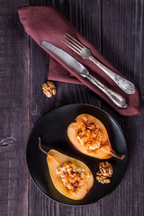 Baked pear on a black plate with cutlery and a brown napkin. Dark background. Top view with copy space for your text