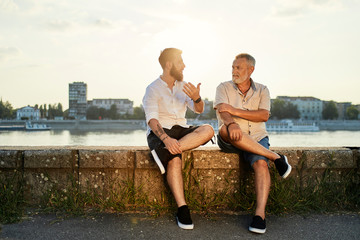 Father and adult son sitting on a wall at the riverside talking