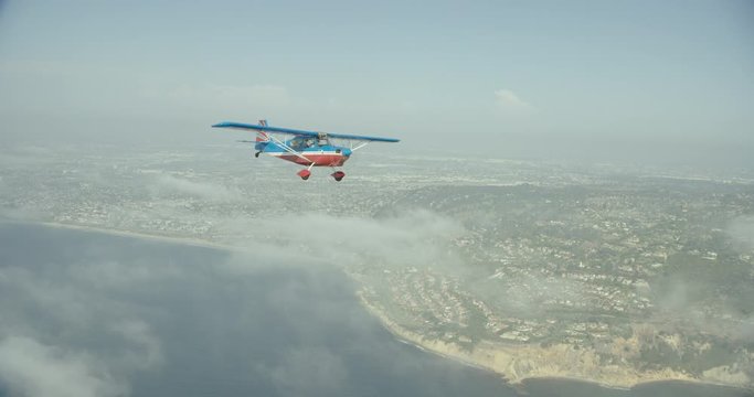 Aerial shot of small aircraft flying over ocean onto land above clouds, day