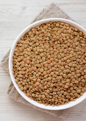 Organic green lentils in a white bowl on a white wooden background, top view. Close-up.