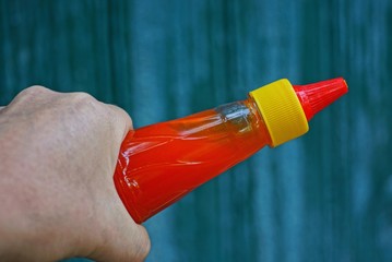 Naklejka premium hand holds a plastic bottle with red ketchup on a green background