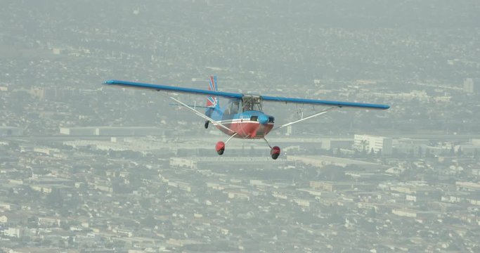 Gloomy helicopter aerial shot of small red and blue seaplane flying over urban landscape, day