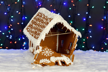 The crashed hand-made eatable gingerbread house, snow decoration, garland background illumination
