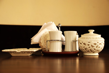 There is a set of white saltshaker and ashtray and tissue holder on a brown classy table great lightning no people