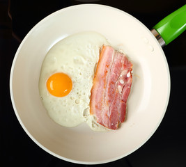 fried egg with bacon and bacon on frying pan