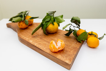 Fresh juicy clementine mandarins, winter time fruits.Half-peeled mandarin and peel on a wooden surface, minimalistic still life. Mandarine or tangerine with leaves on wooden board